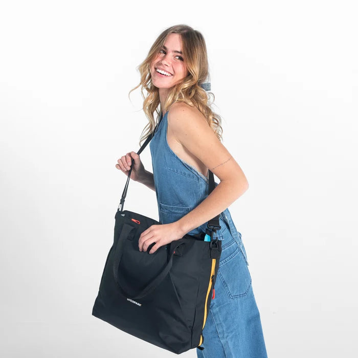A woman wearing a Sherpani Jetsetter Chromatic Back Travel Tote Bag by the crossbody strap  on white backdrop.  #color_chromatic-black