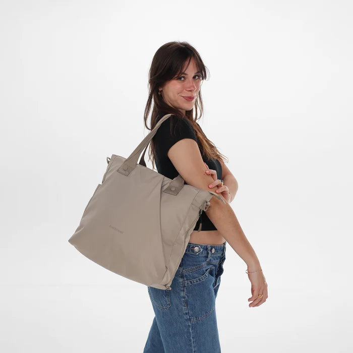A woman wearing a Sherpani Jetsetter Dune Travel Tote Bag on white backdrop.  #color_dune-tan