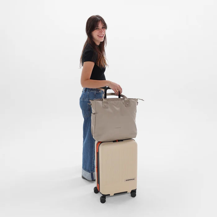 A woman holding a Sherpani Jetsetter Dune Travel Tote Bag on top of a Sherpani Meridian Luggage. 
#color_dune-tan