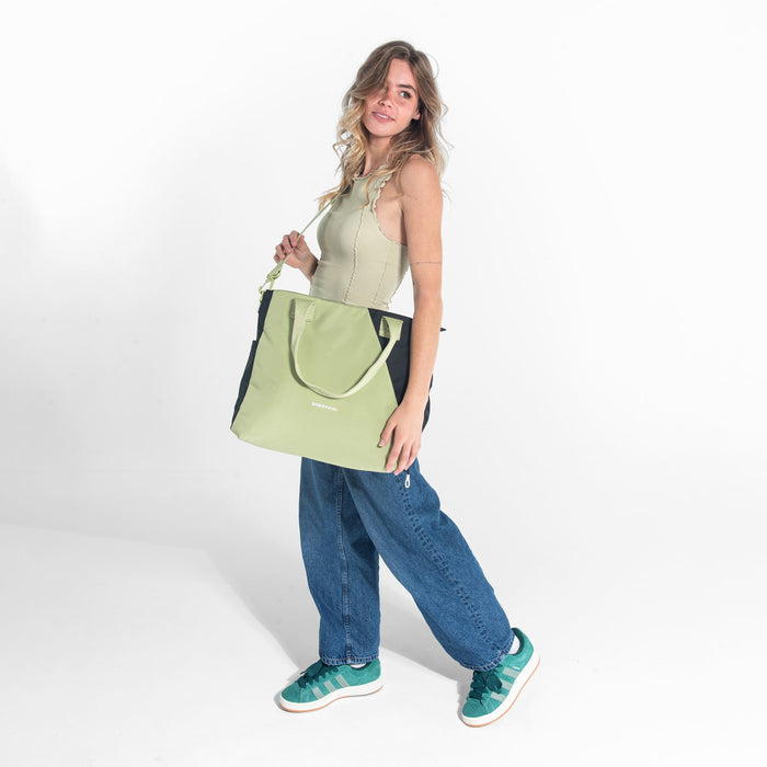A woman wearing a Sherpani Jetsetter Palm Green Travel Tote Bag by the crossbody strap on white backdrop. #color_palm-green