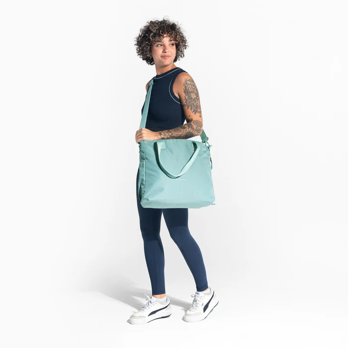 A woman wearing a Sherpani Jetsetter Surf Blue Travel Tote Bag by crossbody strap on white backdrop.  #color_surf-blue