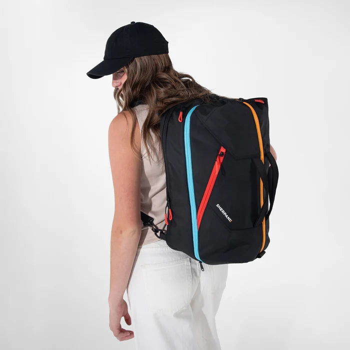 Woman wearing a Sherpani Juno Chromatic Black Duffel Backpack on her back against white backdrop. #color_chromatic-black