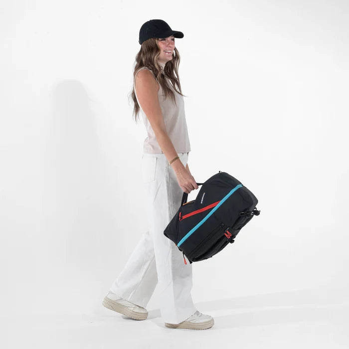 Woman holding a Sherpani Juno Chromatic Black Duffel Backpack by duffle straps against white backdrop. #color_chromatic-black