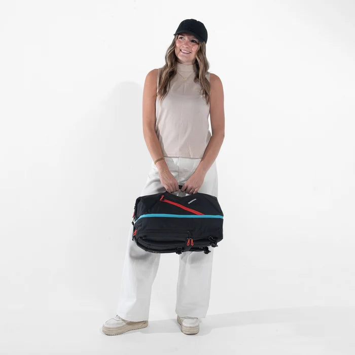 Woman holding a Sherpani Juno Chromatic Black Duffel Backpack by duffle straps against white backdrop. #color_chromatic-black