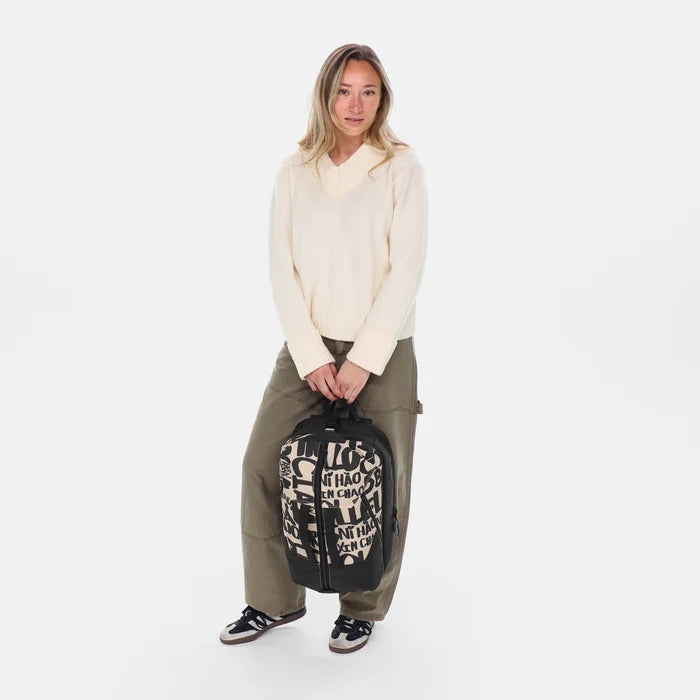 Woman holding a Sherpani Juno Ciao Duffel Backpack by top strap against white backdrop. #color_ciao-print
