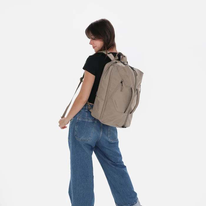 Woman wearing a Sherpani Juno Dune Duffel Backpack on her back against white backdrop. #color_dune-tan