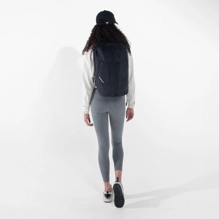 Woman wearing a Sherpani Juno Raven Black Duffel Backpack by shoulder straps against white backdrop. #color_raven-black