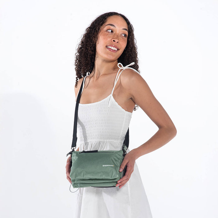 Woman wearing a Sherpani Mei Aloe Mist Green Anti-theft Travel Trio Crossbody around her shoulder against white backdrop.  #color_aloe-mist-green