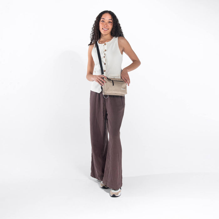 Woman wearing a Sherpani Mei Straw Beige Anti-theft Travel Trio Crossbody around her shoulder against white backdrop.    #color_straw-beige