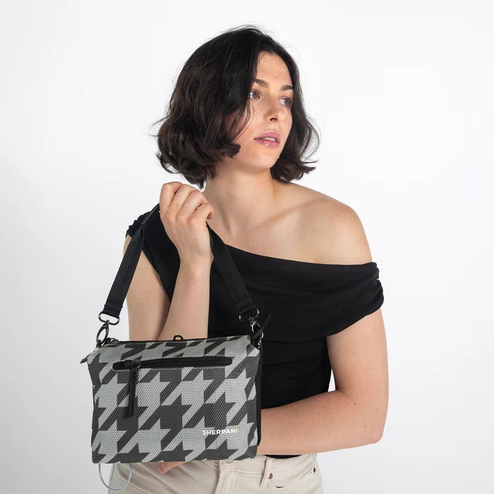 Woman holding a Sherpani Mei Houndstooth Anti-theft Travel Trio Crossbody by the short strap against white backdrop. #color_houndstooth-print