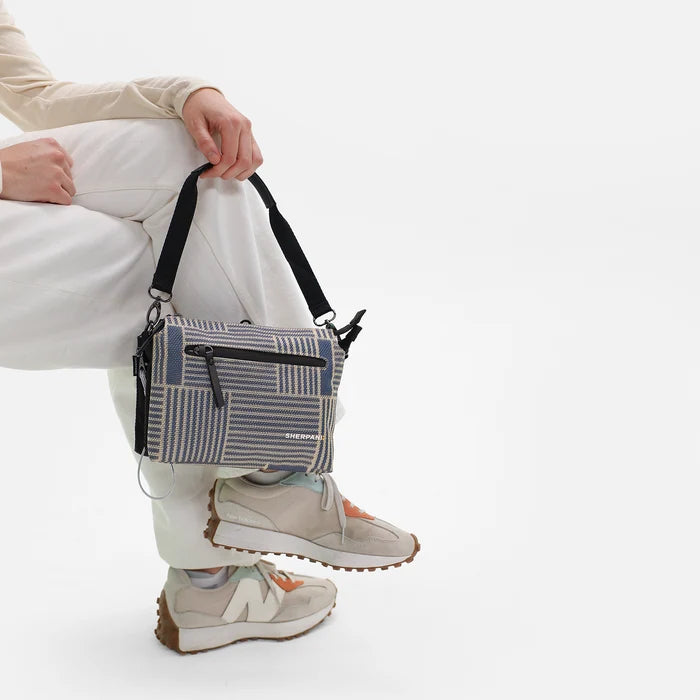 Woman holding a Sherpani Mei Passport Anti-theft Travel Trio Crossbody by the short strap against white backdrop. #color_passport-print