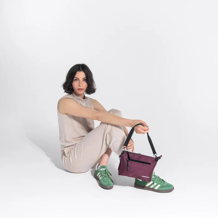 Woman holding a Sherpani Mei Smoky Orchid Anti-theft Travel Trio Crossbody by the short strap against white backdrop. #color_smoky-orchid-pink