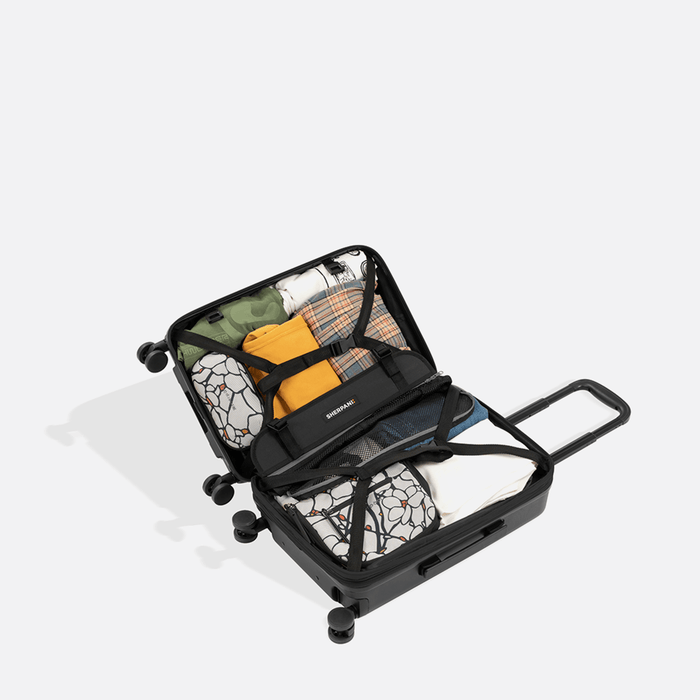 A Sherpani Meridian Black Carry-On Luggage, above view showing fully packed interior on white backdrop.   #color_black