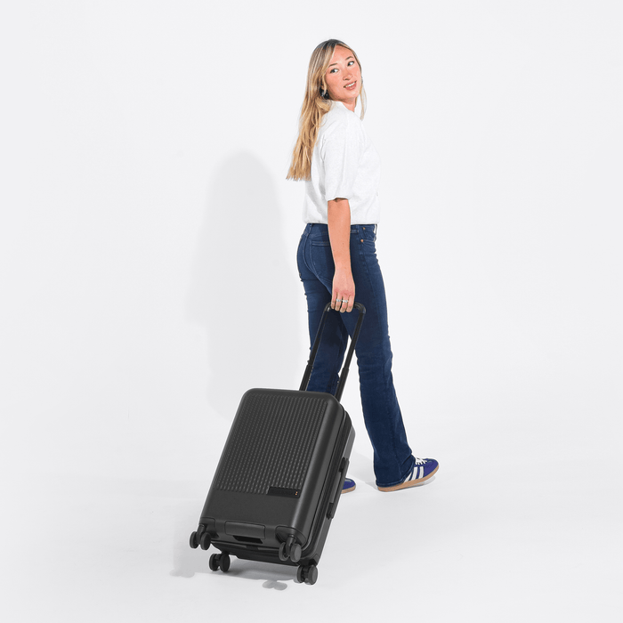 Woman holding a Sherpani Meridian Black Carry-On Luggage by the handle against white backdrop.  #color_black