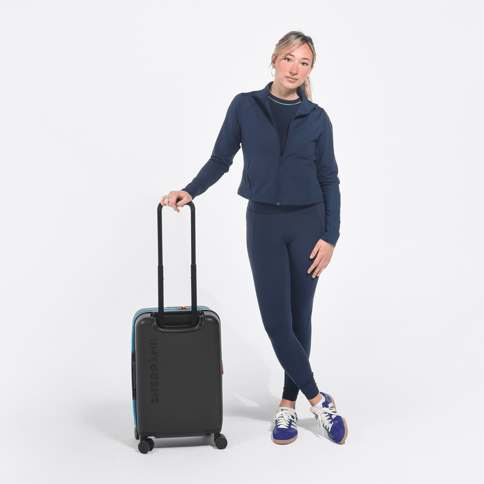 Woman holding a Sherpani Meridian Chromatic Black Carry-On Luggage by the handle against white backdrop.   #color_chromatic-black