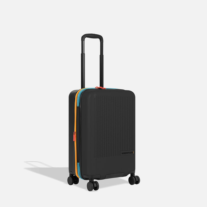 A Sherpani Meridian Chromatic Black Carry-On Luggage, 3/4 view showing zipper and extender against white background.  #color_chromatic-black