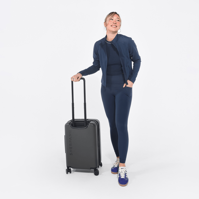 Woman holding a Sherpani Meridian Granite Carry-On Luggage by the handle against white backdrop. #color_granite-grey