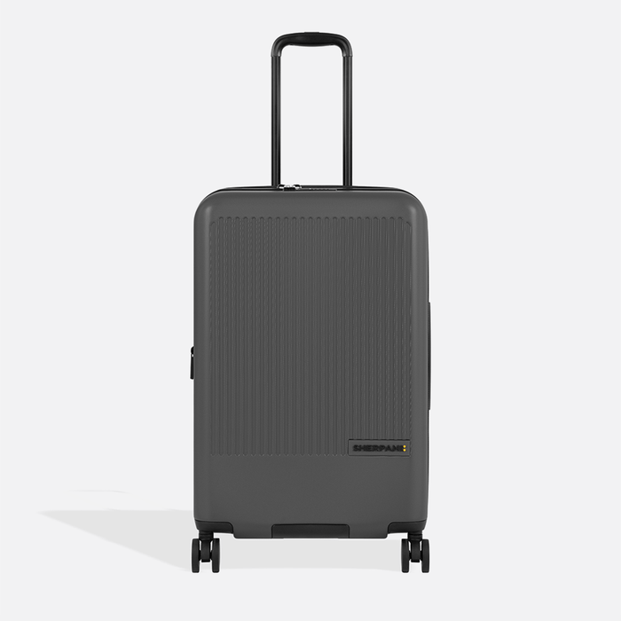 A Sherpani Meridian Granite Checked-Luggage, front view showing handle and zipper extender on white backdrop.    #color_granite-grey
