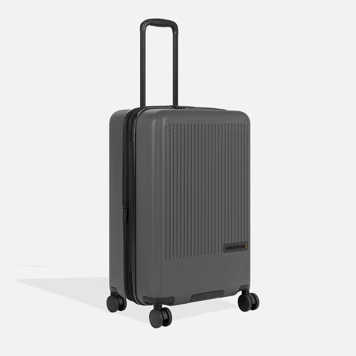 A Sherpani Meridian Granite Checked-Luggage, 3/4 view showing zipper and extender against white background.    #color_granite-grey