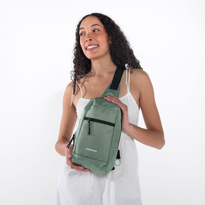 A woman wearing a Sherpani Metro Aloe Mist Green Anti-theft Reversible Sling on her front against a white background.  #color_aloe-mist-green