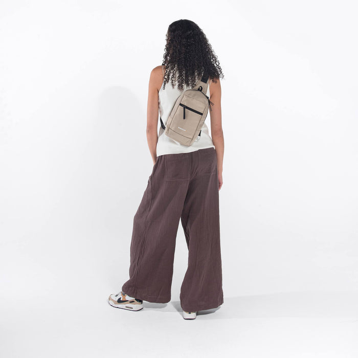 A woman wearing a Sherpani Metro Straw Beige Anti-theft Reversible Sling on her back against a white background.  #color_straw-beige