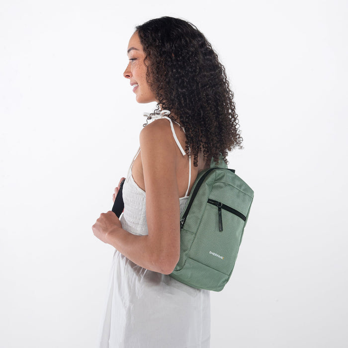A woman wearing a Sherpani Metro Aloe Mist Green Anti-theft Reversible Sling on her back against a white background.  #color_aloe-mist-green