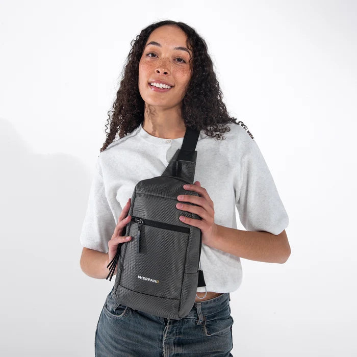 Woman wearing a Sherpani Metro Granite Anti-theft Reversible Sling on her front against white backdrop.  #color_granite-grey