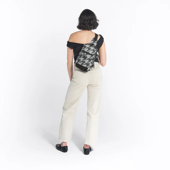 Woman wearing a Sherpani Metro Houndstooth Anti-theft Reversible Sling on her back against white backdrop. #color_houndstooth-print
