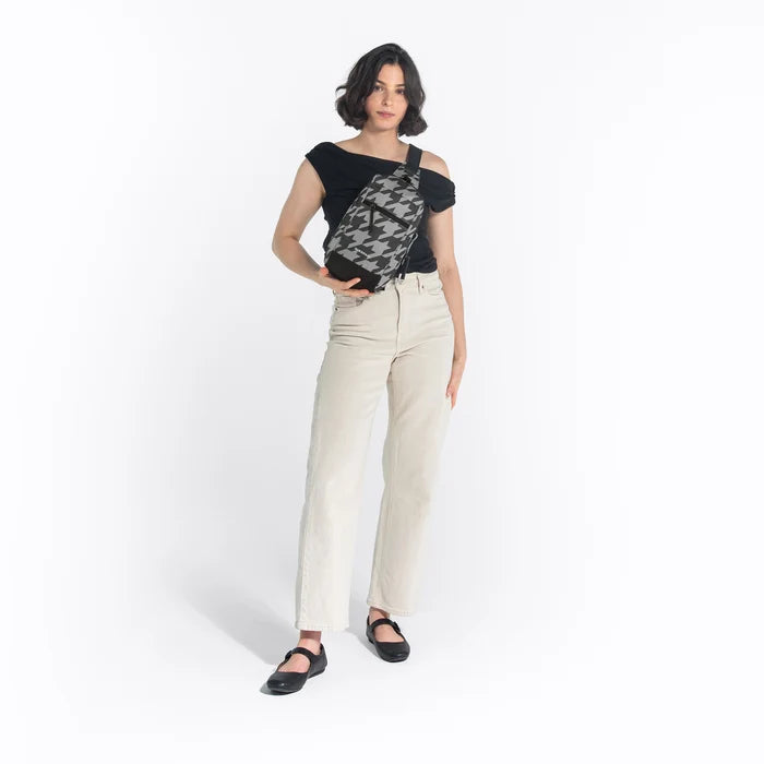 Woman wearing a Sherpani Metro Houndstooth Anti-theft Reversible Sling on her front against white backdrop. #color_houndstooth-print