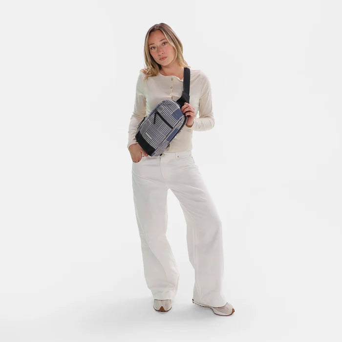 Woman wearing a Sherpani Metro Passport Anti-theft Reversible Sling on her front against white backdrop.#color_passport-print