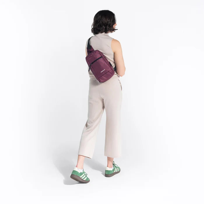 Woman wearing a Sherpani Metro Smoky Orchid Anti-theft Reversible Sling on her back against white backdrop. #color_smoky-orchid-pink