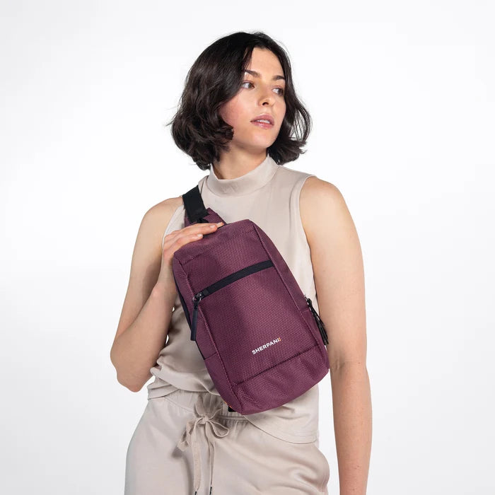 Woman wearing a Sherpani Metro Smoky Orchid Anti-theft Reversible Sling on her front against white backdrop. #color_smoky-orchid-pink