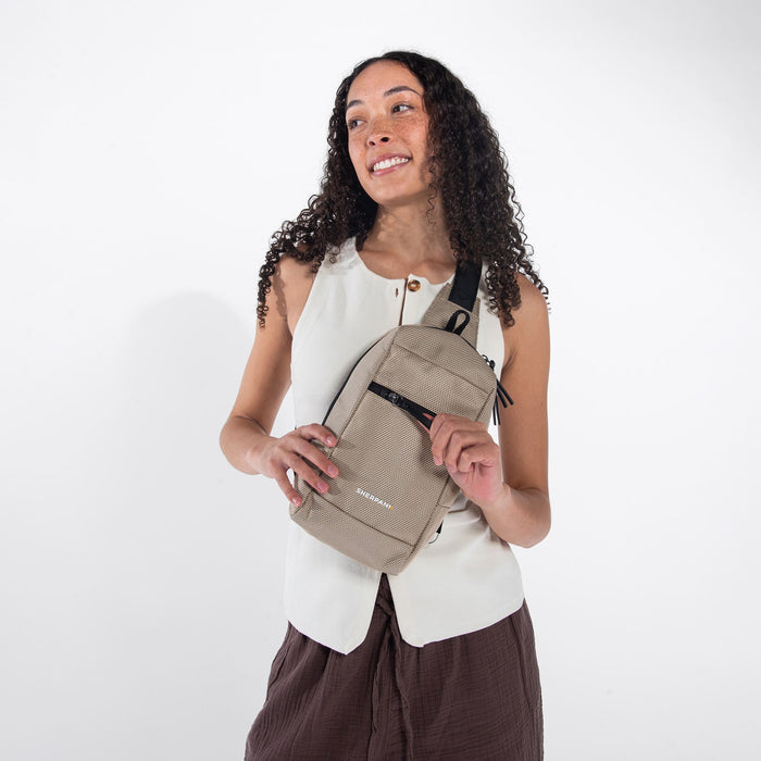 A woman wearing a Sherpani Metro Straw Beige Anti-theft Reversible Sling on her front against a white background.  #color_straw-beige