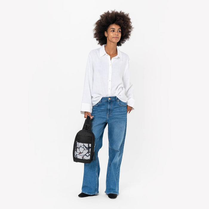 Woman holding a Sherpani Metro Sakura Anti-theft Reversible Sling by adjustable strap against white backdrop. #color_sakura-signature