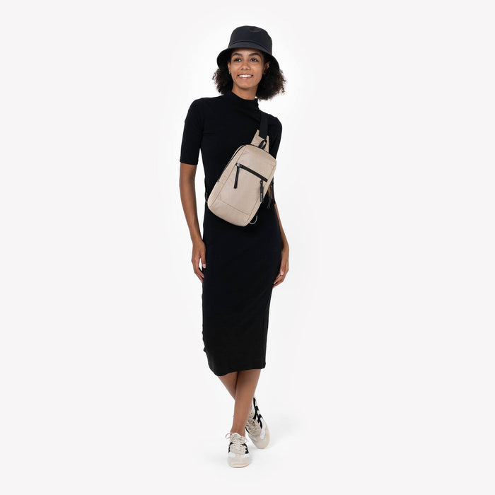 Woman wearing a Sherpani Metro Straw Beige  Anti-theft Reversible Sling on her front against white backdrop. #color_straw-signature