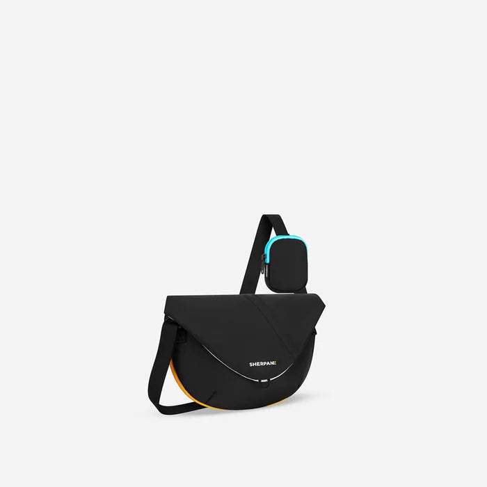A Sherpani Milli Chromatic Black Mini Messenger, 3/4 view showing front flap pocket and strap on white backdrop.  #color_chromatic-black