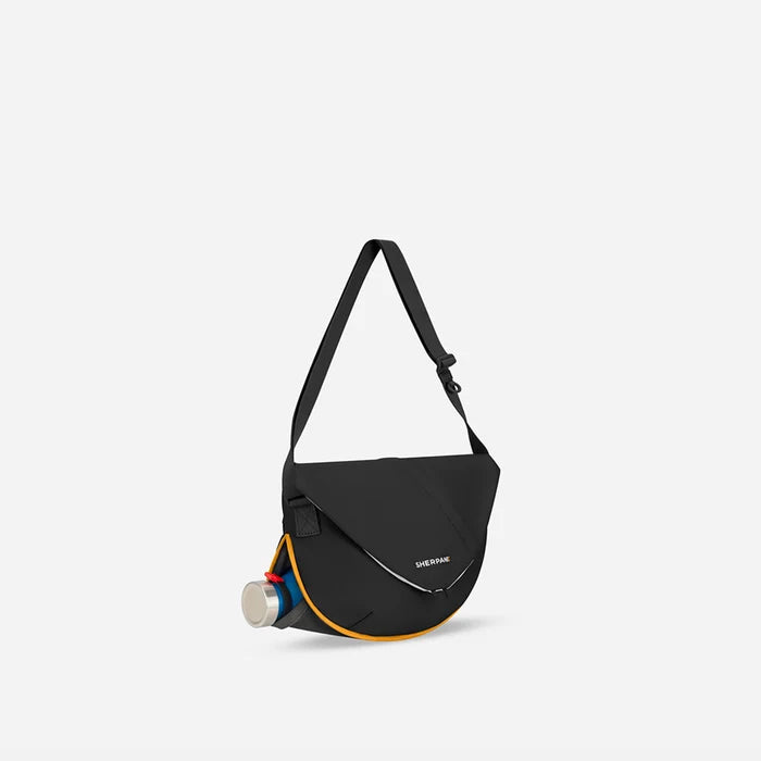 A Sherpani Milli Chromatic Black Mini Messenger, 3/4 view showing front flap pocket and water bottle pocket on white backdrop.   #color_chromatic-black