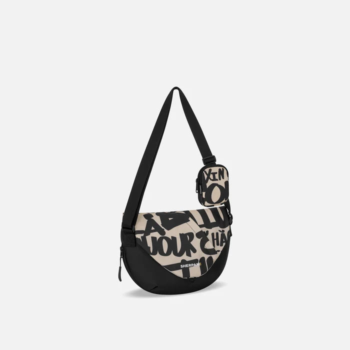 A Sherpani Milli Ciao Mini Messenger, 3/4 view showing front flap pocket and strap on white backdrop.  #color_ciao-print