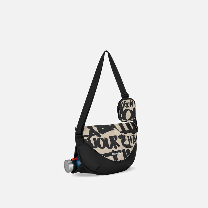 A Sherpani Milli Ciao Mini Messenger, 3/4 view showing front flap pocket and water bottle pocket on white backdrop.  #color_ciao-print