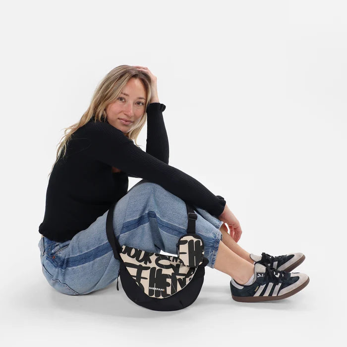 Woman sitting with a Sherpani Milli Ciao Mini Messenger against white backdrop.  #color_ciao-print