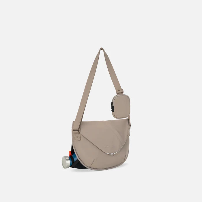 A Sherpani Milli Dune Mini Messenger, 3/4 view showing front flap pocket and water bottle pocket on white backdrop.  #color_dune-tan