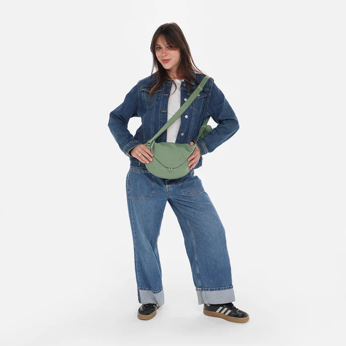Woman wearing a Sherpani Milli Olivine Mini Messenger against white backdrop.  #color_olivine-green