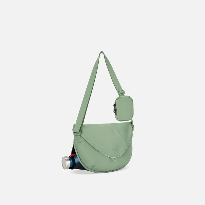 A Sherpani Milli Olivine Mini Messenger, 3/4 view showing front flap pocket and water bottle pocket on white backdrop.  #color_olivine-green