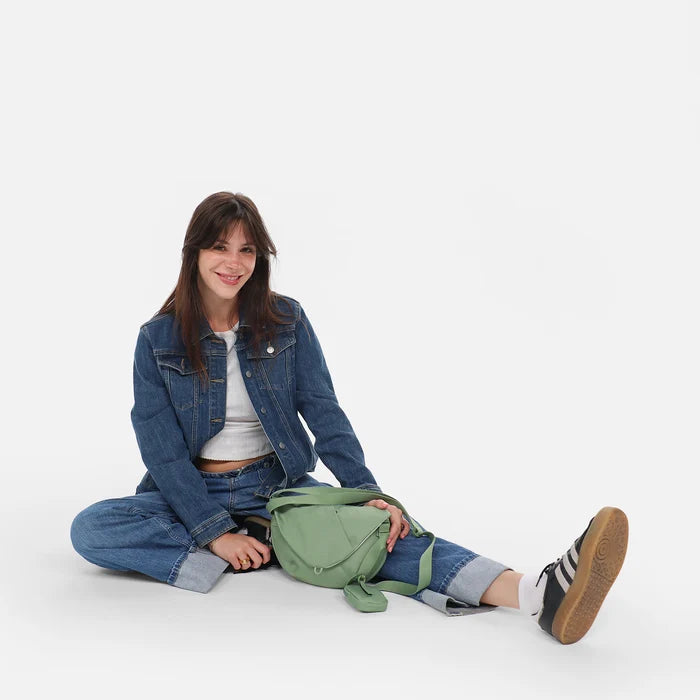 Woman sitting with a Sherpani Milli Olivine Mini Messenger against white backdrop.  #color_olivine-green