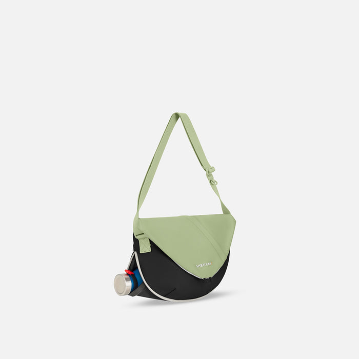 A Sherpani Milli Palm Green Mini Messenger, 3/4 view showing front flap pocket and water bottle pocket on white backdrop. #color_palm-green