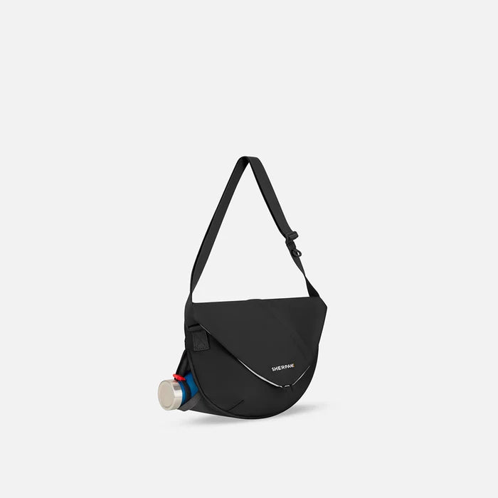 A Sherpani Milli Raven Black Mini Messenger, 3/4 view showing front flap pocket and water bottle pocket on white backdrop.   #color_raven-black