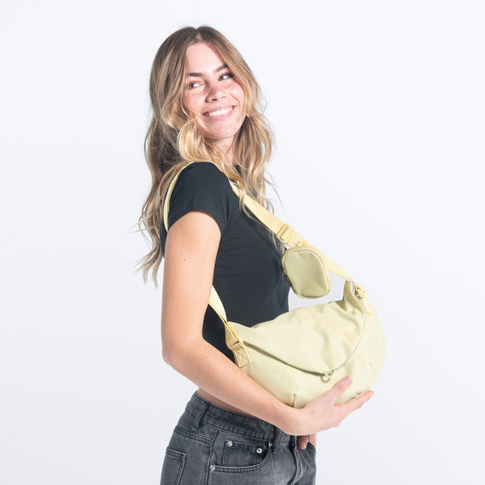 A woman wearing a Sherpani Milli Sol Yellow Mini Messenger on her shoulder against a white background.  #color_sol-yellow