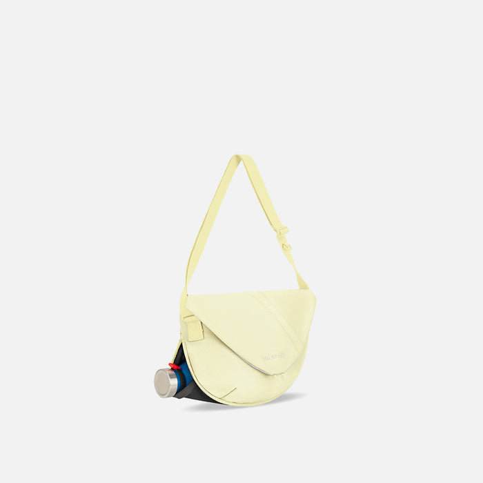 A Sherpani Milli Sol Yellow Mini Messenger, 3/4 view showing front flap pocket and water bottle pocket on white backdrop. #color_sol-yellow