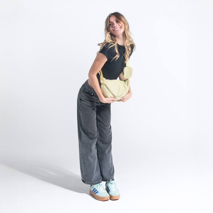 A woman holding a Sherpani Milli Sol Yellow Mini Messenger against a white background.  #color_sol-yellow