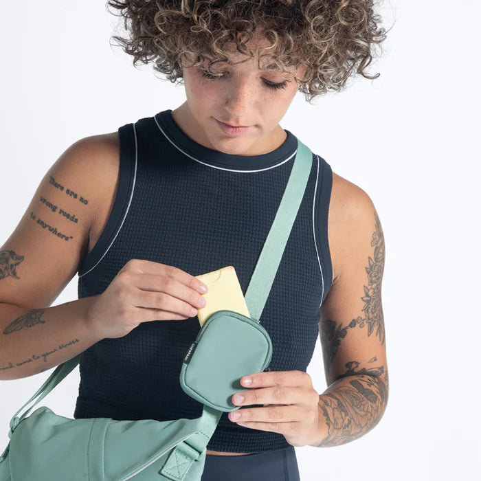 Woman placing a hand sanitizer into a Sherpani Milli Surf Blue Mini Messenger against white backdrop.  #color_surf-blue